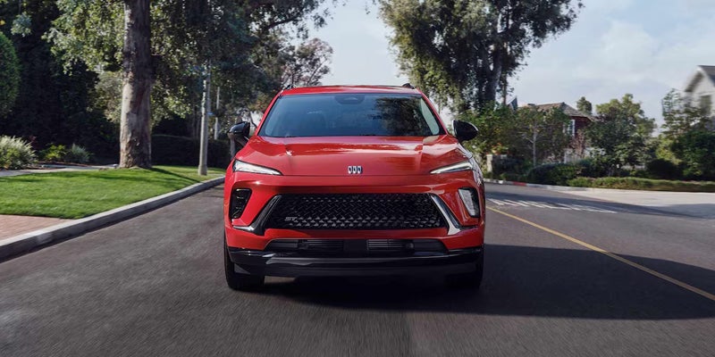 Red Buick Envision driving along a tree-lined residential street.